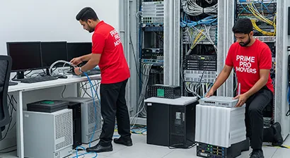 Movers packing IT hardware, monitors, and routers in a tech office during secure office relocation